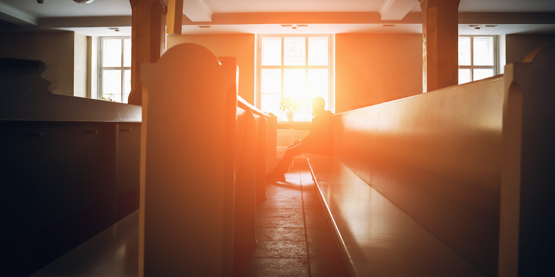 Silhouette of man praying in church in sunset light, toned